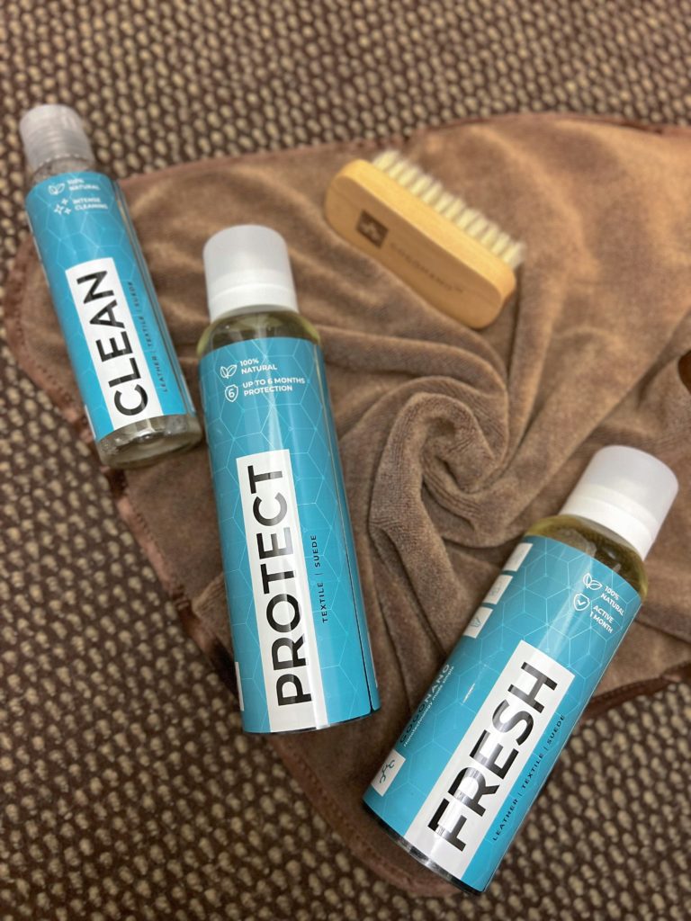 タオルの上に置かれた青いラベルのケア用ボトル3本とブラシ。ルイヴィトンバッグのシミ予防とメンテナンス用品のイメージ。