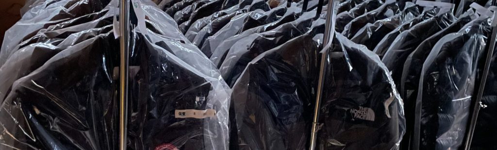 ひらいしやの保管サービスでハンガーにかけられたノースフェイスダウン。通気性の良い不織布カバーに包まれ、多数のダウンジャケットが整然と並んでいる。