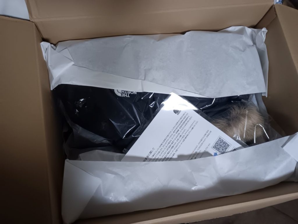 ダンボールの中に梱包されたノースフェイスダウンが見える写真。なにやら手紙も添えられている。